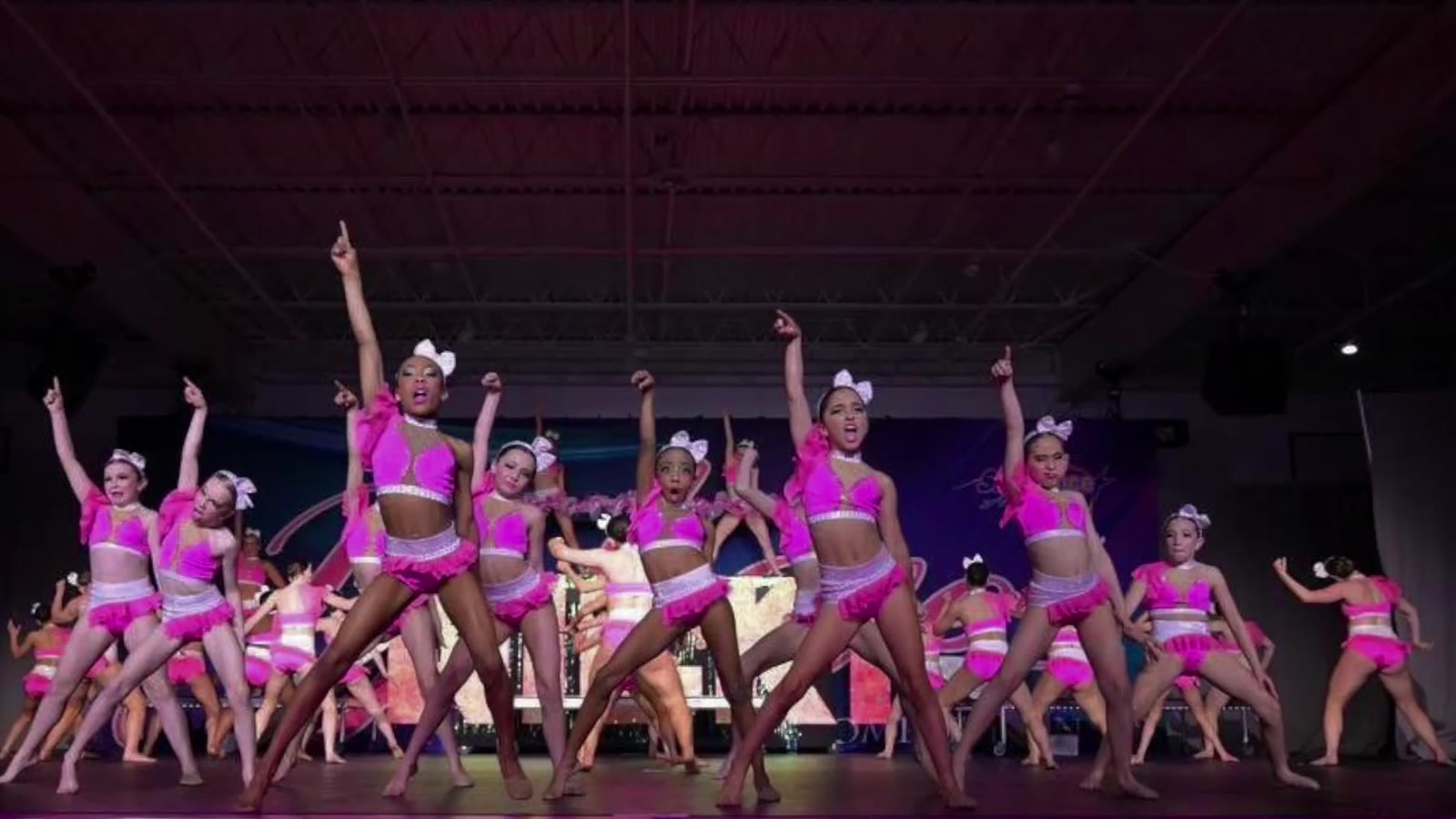 Kay's Act II competitive team performing on stage in hot pink costumes